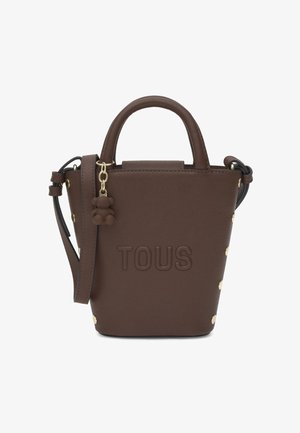 Bolso TOUS de cuero marrón con asas superiores, correa de hombro ajustable, tachuelas doradas en los laterales y charm llavero de oso de peluche.