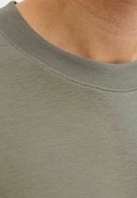 Bombažna majica olivno zelene barve z okroglim izrezom. Ima gladko teksturo in rebrasto obrobo na vratnem izrezu, z minimalnimi detajli šivov.