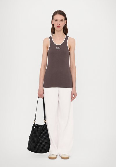 Brūns ribots topiņš ar baltu apmalīti un "MM" logotipu, kombinēts ar brīvām baltām biksēm un melnu austu somu ar plecu siksnu.