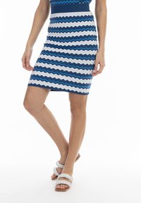 Strickrock mit Zickzackmuster in Blau, Weiß und Marineblau; figurbetontes Design und gerippter Bund. Getragen mit weißen Riemchensandalen.