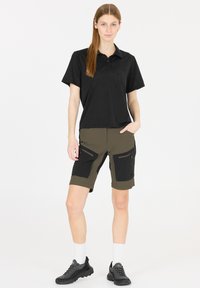 Svart polo-shirt med krage, parat med olivgröna shorts med svarta accentfickor. Modellen bär svarta sneakers och vita strumpor.