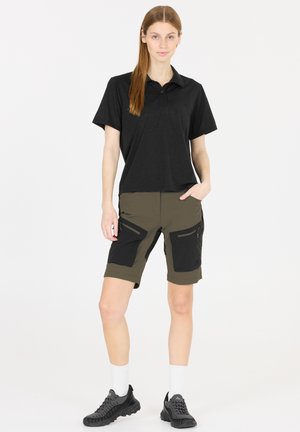 Svart polo-shirt med krage, parat med olivgröna shorts med svarta accentfickor. Modellen bär svarta sneakers och vita strumpor.