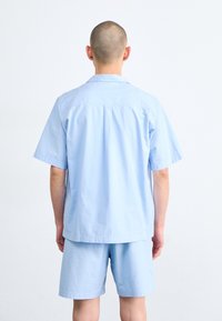 Světlomodrá košile s krátkými rukávy a límcem a odpovídající šortky. Tkanina má na pohled texturu a nabízí pohodlný střih pro neformální nošení.