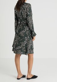 Langärmliges Kleid mit einem Sternmuster in Schwarz, Grün und Weiß, mit gestuftem Design, schwingendem Saum und weicher Stoffbeschaffenheit.