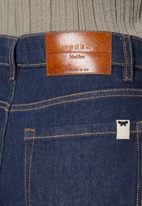 Dunkelblaue Jeans aus Denim mit einem braunen Lederetikett, auf dem "WEEKEND MaxMara" steht. Mit kontrastierenden gelben Nähten und einem kleinen weißen Etikett.