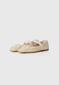 Ballerines en cuir beige avec un design à bout rond, présentant un devant plissé, deux straps croisés et une semelle plate.