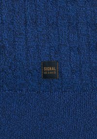 Kék kötött szövet, textúrált mintával. Egy kis fekete címke van rávarrva, arany betűkkel "SIGNAL LOT S-44-25" felirattal.