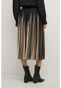 Pleated midi skirt featuring alternating black and beige stripes, with a fitted waistband and a flowing finish. Black ankle boots complete the look.
