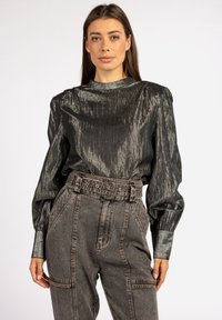 Metallisch zwarte blouse met lange mouwen en een gestructureerde kraag, met gather op de schouders, gecombineerd met hoog-waisted grijze denim broek met een riem om de taille.