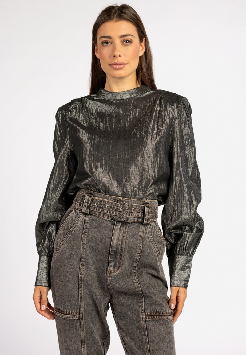 Metallisch zwarte blouse met lange mouwen en een gestructureerde kraag, met gather op de schouders, gecombineerd met hoog-waisted grijze denim broek met een riem om de taille.