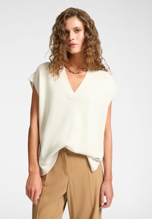 Top de pico en crema con mangas cortas; tejido suave y texturizado; combinado con pantalones beige; corte relajado; destacado por un ligero drapeado en el dobladillo.