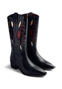 Botas de vaquero de cuero negro con bordados en forma de alas en rojo y beige, con puntas afiladas, presentadas una al lado de la otra sobre un fondo blanco.