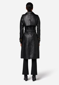 Zwarte leren trenchcoat met een ceintuurlengte, brede kraag en schouderepauletten. Beschikt over een gladde afwerking en een rugventilatie voor gemakkelijke beweging.