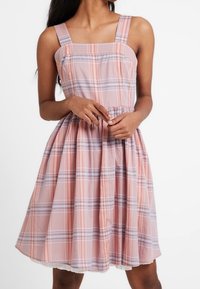 Różowa sukienka w kratkę, wykonana z lekkiego materiału, z kwadratowymi ramiączkami, dopasowanym gorsem i rozkloszowaną spódnicą z koronkowym wykończeniem u dołu.