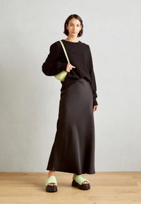 Sudadera negra de gran tamaño, falda de satén negra elegante, bolsa cruzada verde mini y sandalias verdes gruesas con una correa texturizada.