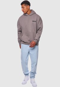 Šedá oversized mikina s přední kapsou a textem "DROPSIZE". Oblečení doplňují světle modré volné kalhoty a bílé tenisky.