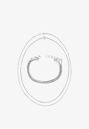 Zilveren ketting- en armbandset met drie dunne kettingen met een gladde textuur en een karabijnsluiting, in lagen gerangschikt.