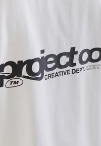 Bijela pamučna majica s bold crnim tekstom koji glasi "project co. CREATIVE DEPT." s ovalnim simbolom zaštitnog znaka.
