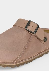 Μαλακό ροζ σουέτ παπούτσι slip-on με ρυθμιζόμενο δερμάτινο λουράκι και μεταλλική αγκράφα, φελλό σόλα και λεπτομέρεια κουμπιού με το λογότυπο Birkenstock.
