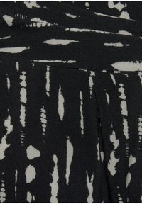 Černá tkanina s texturovaným vzorem nepravidelných bílých tvarů a linií, vytvářející výrazný kontrast s hladkým povrchem.
