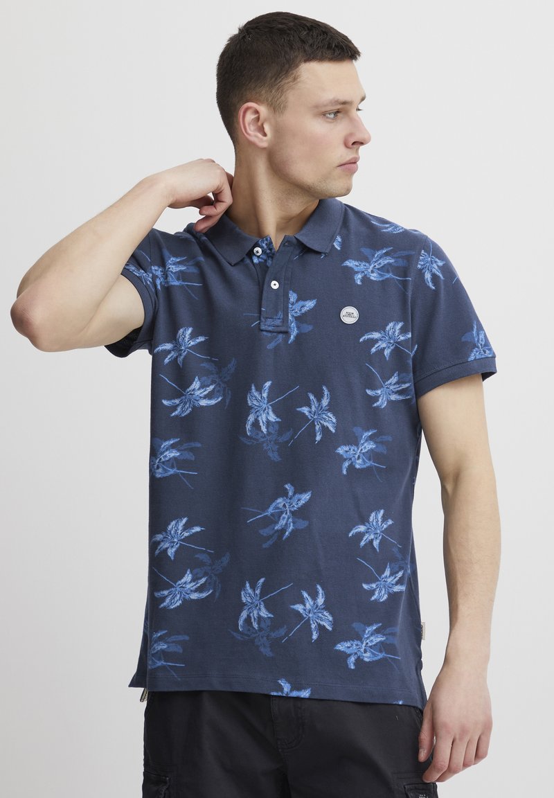 Marineblå polo med blomstermønster i blått, tre-knappslukking og logo-patch. Korte ermer og rett nederkant. Laget av bomull.