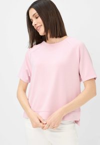 Kortærmet pink sweatshirt med rund halsudskæring, ribbet tekstur og sideslids. Har en subtil dekorativ metalaccent i kanten.
