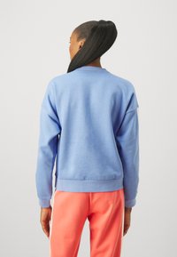 Blå sweatshirt med långa ärmar och ribbade mudd. Klassisk skärning med rundad halsringning, kombinerad med rosa träningsbyxor med sidostripes.