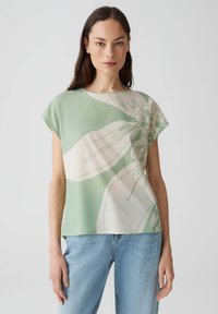 Blusa verde chiaro con stampa floreale in crema, caratterizzata da una vestibilità rilassata, scollatura rotonda e maniche corte, realizzata in tessuto morbido.