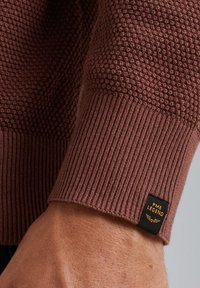 Brauner strukturierter Pullover mit gerippten Bündchen. Enthält ein schwarzes und goldenes Etikett mit der Aufschrift "PME Legend" am Bündchen.