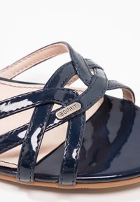 Sandale en cuir verni bleu marine avec des bretelles croisées et une petite étiquette métallique du logo Esprit sur la sangle avant.