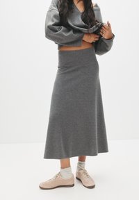 Grå strikket lang nederdel med høj talje, parret med en matchende cropped sweater og beige sneakers. Blød tekstur, enkelt design.
