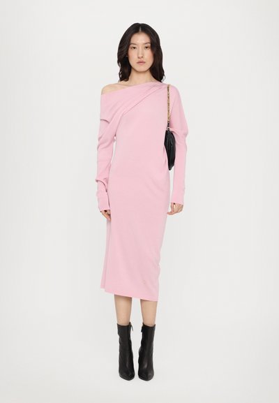Rochie roz cu umeri descoperiți, realizată dintr-un material moale, având mâneci lungi și un design ajustat. Asortată cu cizme negre până la glezne și o geantă mică neagră.