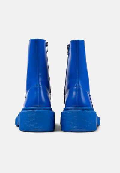 Stivali alla caviglia blu realizzati in materiale lucido con suola spessa. Dettaglio con zip sul retro, progettati per un look aderente.