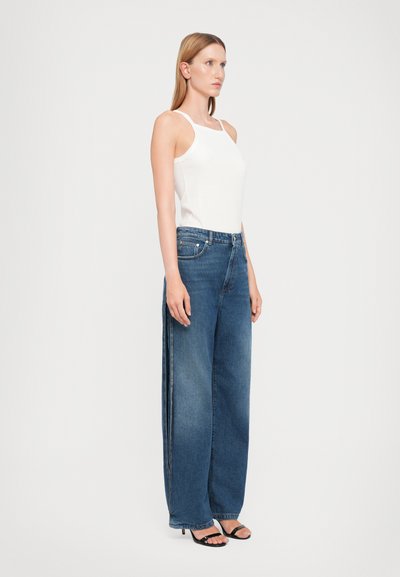 Jean en denim bleu à jambe large avec une taille haute, présentant des coutures latérales élégantes et un haut sans manches blanc décontracté. Tissu léger et texturé.