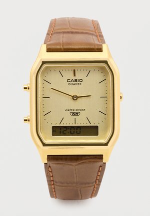 Goldfarbene, quadratische Casio Quarzuhr mit einem beigen Zifferblatt, schwarzen Markierungen und einem digitalen Display. Armband aus braunem Leder mit Krokodilprägung.