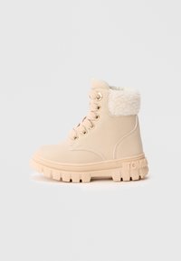 Beige ankelstøvel med tykk gummisåle, polstret ankelkrage foret med hvit fleece, og beige snørebånd med gulløyestykker.