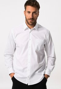 Camisa blanca de manga larga con un diseño sencillo, presenta un bolsillo en el pecho, cierre de botones y un cuello clásico. Tela suave y ligera.