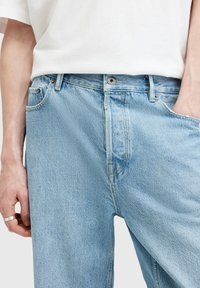 Jeans de mezclilla azul claro con un corte relajado, que presentan un ligero efecto de arrugas, un diseño clásico de cinco bolsillos y cierre de botón metálico.