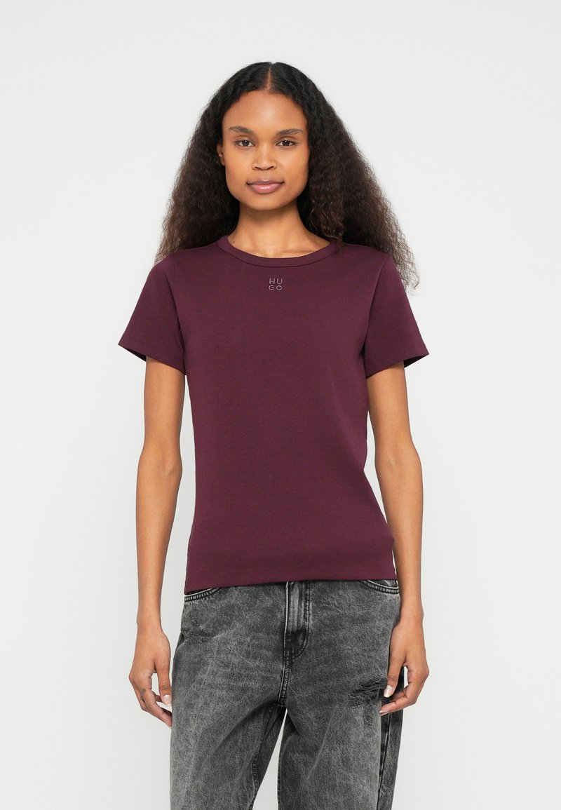 Κοντομάνικο, εφαρμοστό μπλουζάκι από βαμβάκι σε σκούρο μωβ με στρογγυλή λαιμόκοψη και διακριτικό λογότυπο «HUGO» στο κέντρο. Γκρι, φθαρμένο τζιν.