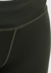 Leggings verde scuro con una texture liscia, dotati di una vita alta e cuciture a contrasto lungo le giunture.