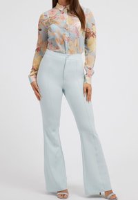 Blouse transparente à motifs floraux dans des tons pastel, associée à un pantalon évasé bleu clair ajusté, présentant une texture lisse et des coutures apparentes.
