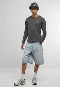 Felpa grigia a maniche lunghe con ancora ricamata, abbinata a pantaloni corti di denim azzurri. Indossata con calze bianche e scarpe da ginnastica argentate.
