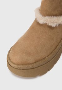 Tan ruskinds ankleboot med en blød faux fur kant og en tyk gummisål med prægede detaljer langs kanten.