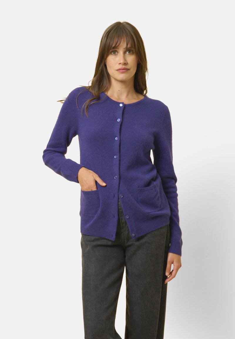 Lila ullcardigan med rund halsringning, knappstängning, två framfickor och ribbade ärmslut. Mjuk textur och minimalistisk design.