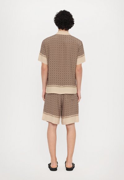 Chemise à manches courtes à motifs marron et shorts assortis, tous deux avec des accents beiges aux poignets et à l'ourlet, fabriqués dans un tissu léger et d'un ajustement décontracté.