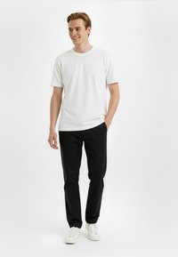 Valkoinen puuvillainen crew neck -t-paita, joka on yhdistetty mustiin housuihin ja valkoisiin lenkkareihin, sisältäen rennon istuvuuden ja lyhyet hihat.