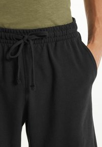 Černé tepláky mají elastický pas se šňůrkou, boční kapsy a měkkou, strukturovanou tkaninu.