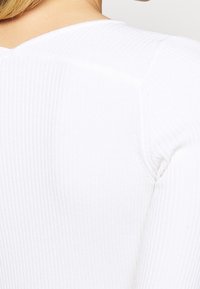 Weißes, geripptes Langarmtop mit weitem Halsausschnitt und strukturiertem Stoff, enger Passform und sichtbaren Nahtdetails.