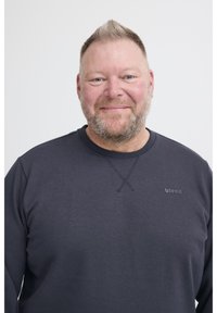 Mosolygó, középkorú férfi, rövid szőke hajjal és szakállal, sötétszürke pulóverben, amelyen a "blend" logó látható, a fehér háttér előtt áll.