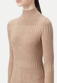 Beige ribbad stickad tröja med hög krage. Har växlande vertikala och horisontella ribbmönster. Långa ärmar, figurnära design.